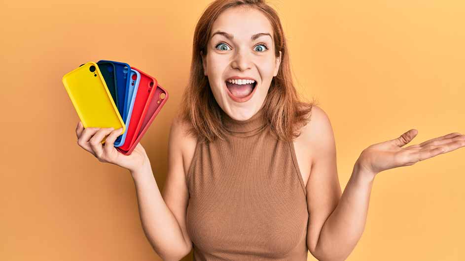 Een vrouw lacht en houdt telefoonhoesjes in de kleuren geel, blauw en rood vast tegen een oranje achtergrond.