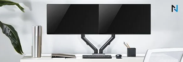 Twee zwarte monitoren op een bureau met een toetsenbord, muis, pennenhouder en een stapel boeken tegen een witte achtergrond.