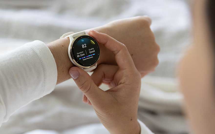 Een persoon bekijkt slaapkwaliteit en duur op een witte Garmin smartwatch, ontspannen in een huiselijke omgeving.