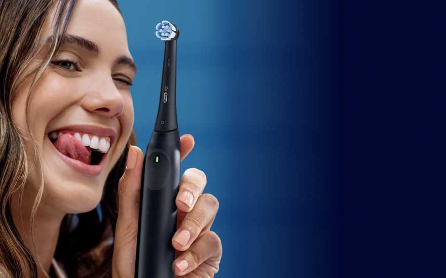 A young woman smiles and holds up a black electric toothbrush against a blue background in a polished product-style image