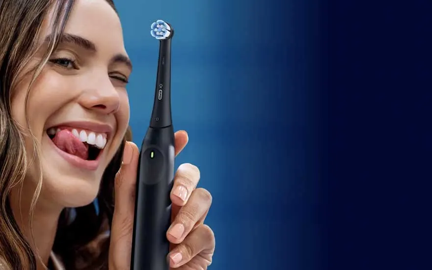 A young woman smiles and holds up a black electric toothbrush against a blue background in a polished product-style image