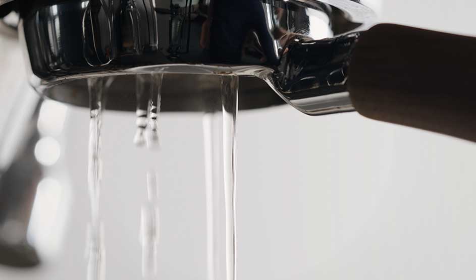 Uit een metalen filterhouder van een espressomachine stroomt water naar beneden. Het merk is niet zichtbaar op deze afbeelding.