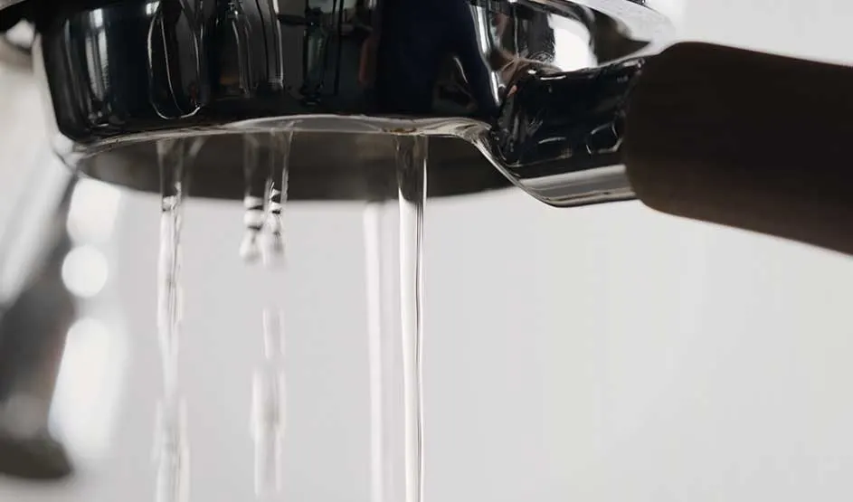 Uit een metalen filterhouder van een espressomachine stroomt water naar beneden. Het merk is niet zichtbaar op deze afbeelding.