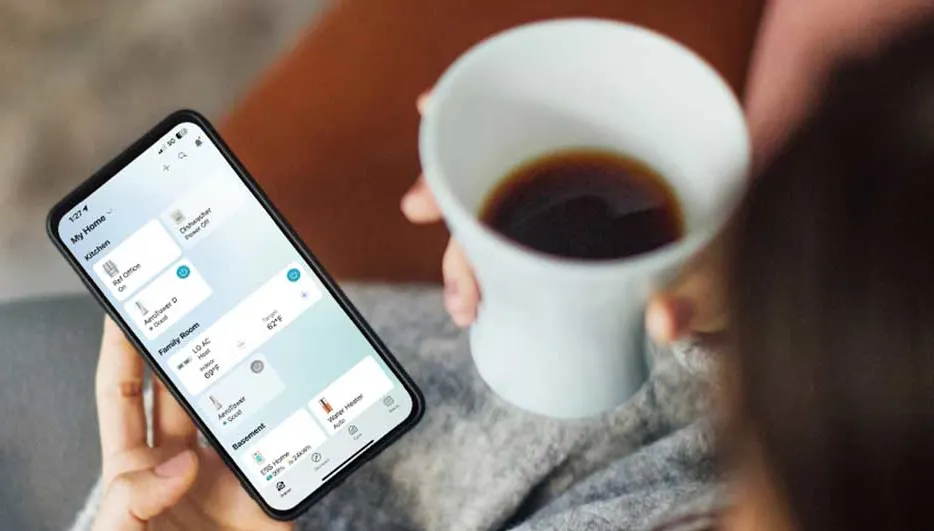 Persoon ontspant met koffie en bekijkt de LG ThinQ-app op een smartphone voor verbonden apparaten thuis.