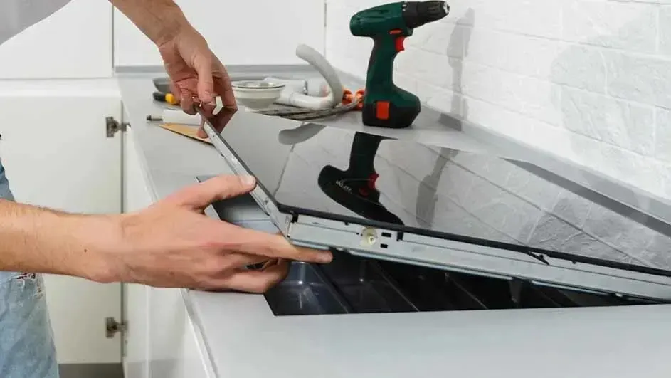 Monteur plaatst een glaskeramische kookplaat in het werkblad; gereedschap ligt klaar, waaronder een accuboormachine en kabels.