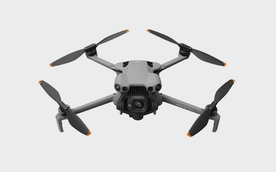 Een vierkante grijze drone met oranje details wordt van bovenaf getoond, op een witte achtergrond met duidelijke lijnen. 