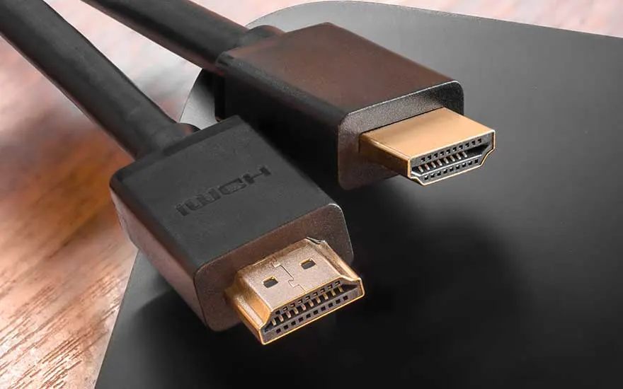 Close-up van zwarte HDMI-kabel met gouden connectoren op houten oppervlak, toont hoogwaardige kabelkwaliteit.