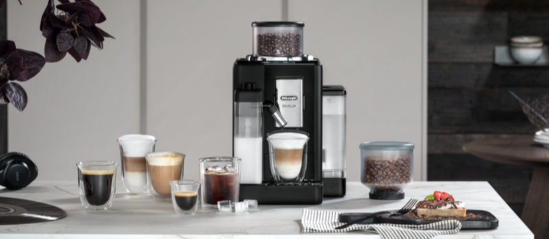 Een koffiemachine met koffiebonen en melk, omringd door verschillende glazen met koffie en een bord met eten.