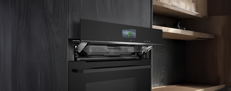 Zwarte oven met digitaal scherm, in een houten keukenkast met open schappen.