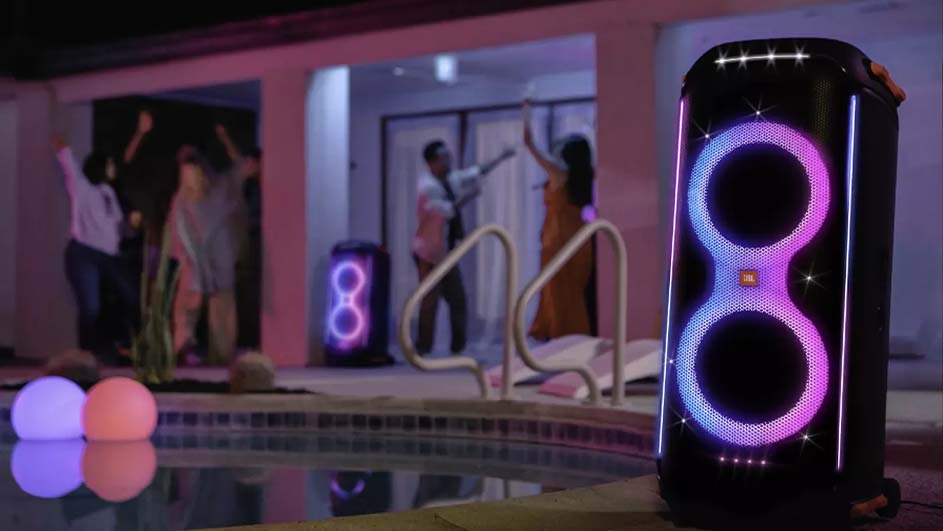 Een feestje bij een zwembad met luidsprekers met gekleurde lichten. Mensen dansen op de achtergrond. Twee ronde lampen reflecteren in het water.