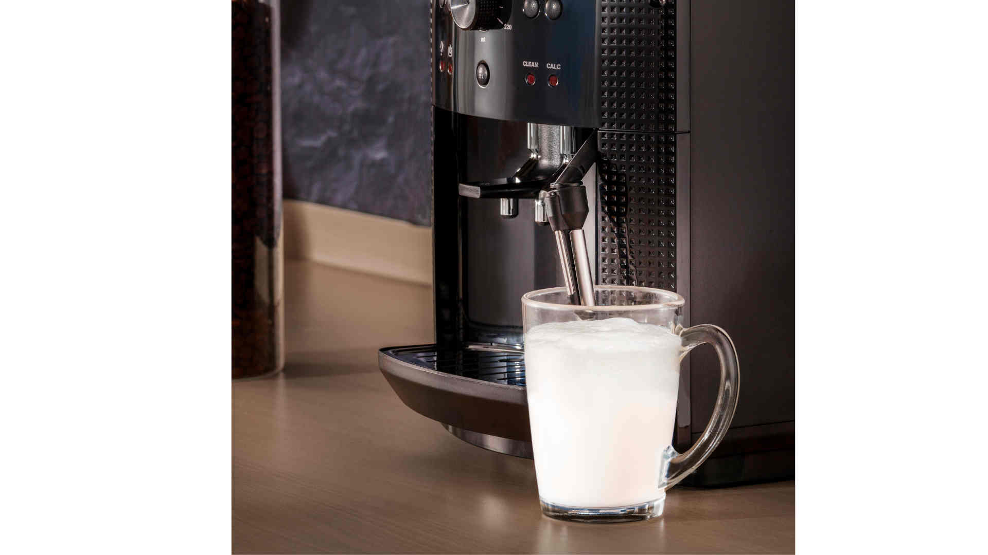 Een zwarte koffiemachine vult een glazen beker met witte vloeistof op een houten aanrecht.