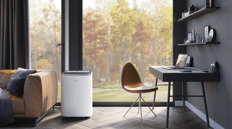 Woonkamer met bank, bureau, stoel en luchtreiniger bij een groot raam met uitzicht op herfstbomen.