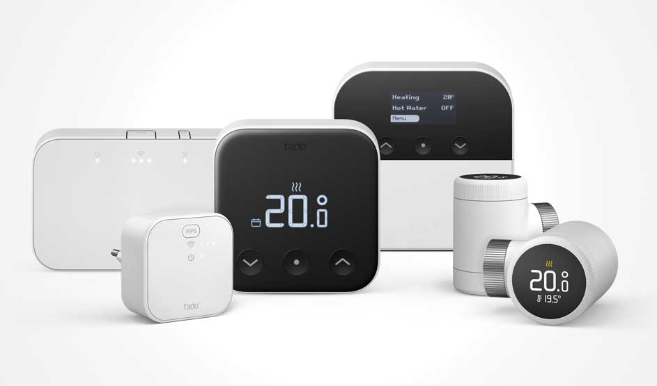 Een set witte en zwarte tado-thermostaten en radiatorknoppen met displays, plus een kleine wifi-bridge, opgesteld op een lichte achtergrond.