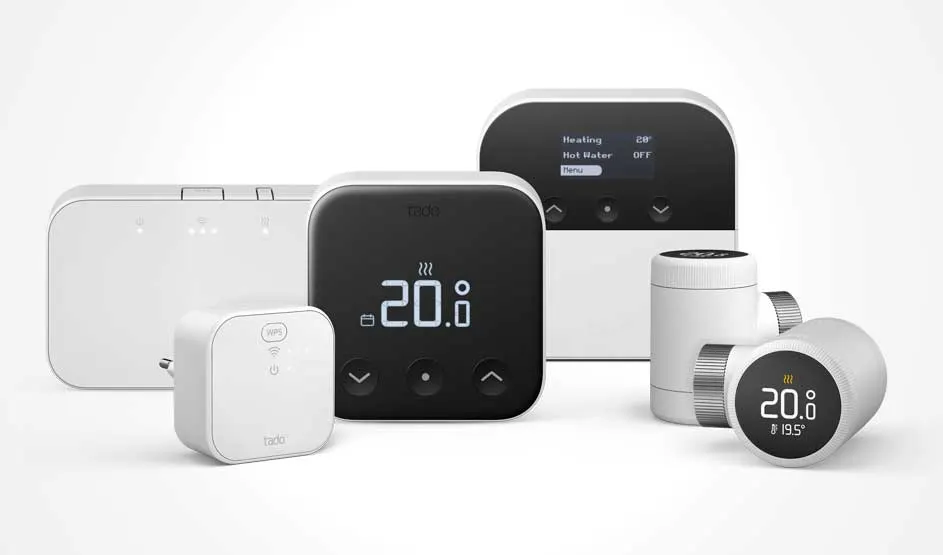 Een set witte en zwarte tado-thermostaten en radiatorknoppen met displays, plus een kleine wifi-bridge, opgesteld op een lichte achtergrond.