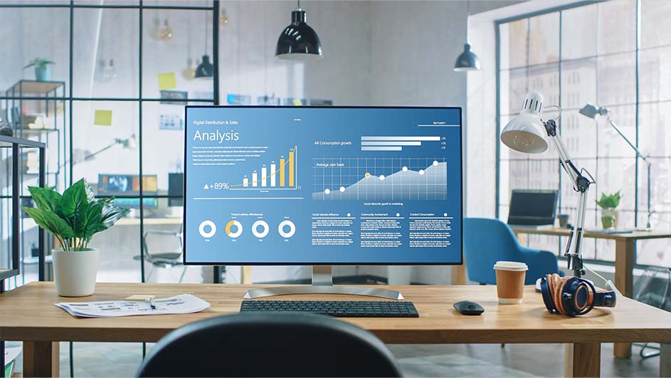 Kantoor met bureau waarop een computer met grafieken, toetsenbord, koptelefoon en een plant staan.