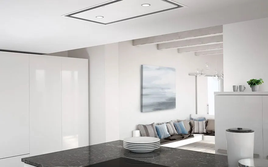 Bright white kitchen with dark countertop, stacked plates, view of a cosy seating nook with cushions and soft abstract art.