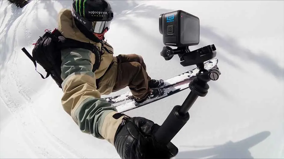 Een persoon zit op een snowboard in de sneeuw, met een camera bevestigd aan een statief voor hen.