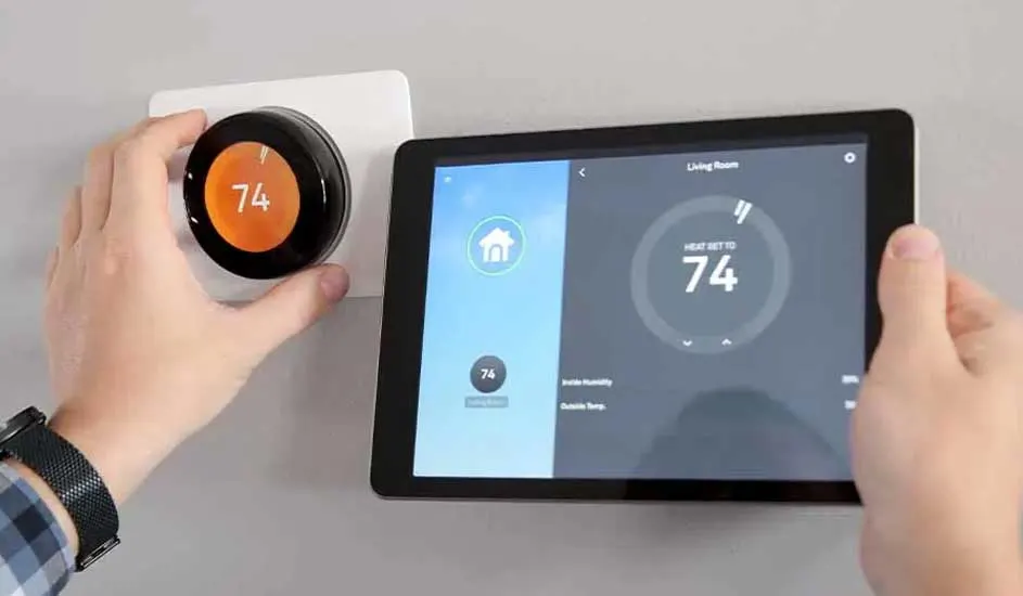 Hands adjust a round, orange-centered thermostat and a tablet showing a similar digital display, both reading "74".