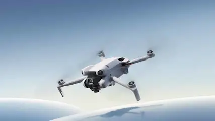 Een witte drone met vier propellers vliegt tegen een blauwe lucht boven een wit oppervlak.