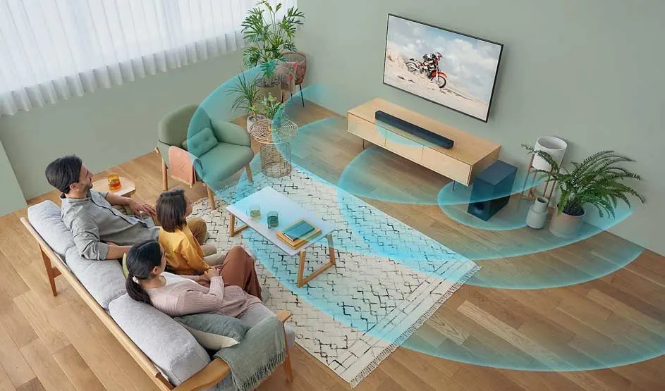 A family sits on the couch facing the TV; blue waves show how the sound spreads through the living room.