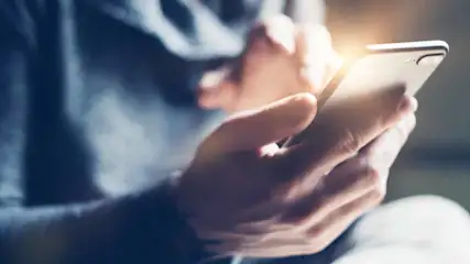 Een persoon in een blauw shirt gebruikt een witte smartphone met één hand.