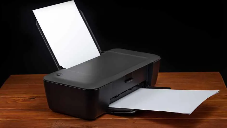 Een zwarte printer staat op een houten tafel tegen een zwarte achtergrond, met wit papier erin en eruit.