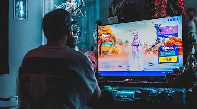 Een persoon zit in een kamer vol verzamelobjecten en speelt Fortnite op een groot Sony televisiescherm met kleurrijke verlichting.