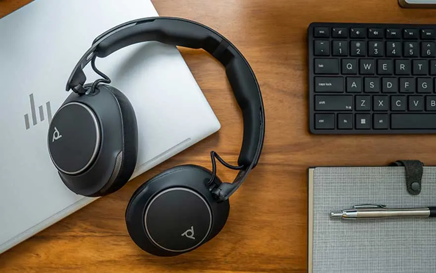 Grote over-ear headset ligt op een houten bureau naast laptop, toetsenbord en notitieboek, klaar voor werk of concentratie.