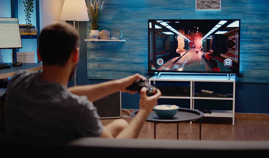 Een man speelt een videogame met controller voor de tv in een gezellige woonkamer met blauwe muur.