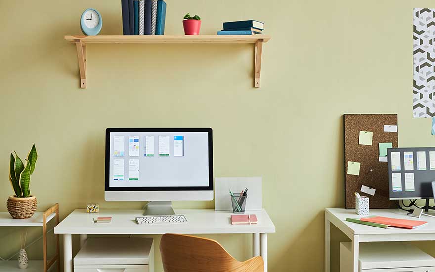 Een nette thuiswerkplek met computer, boeken en planten op een witte tafel.