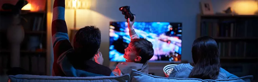 Een gezin zit op de bank en speelt of kijkt enthousiast naar een videogame op tv in een gezellige kamer.