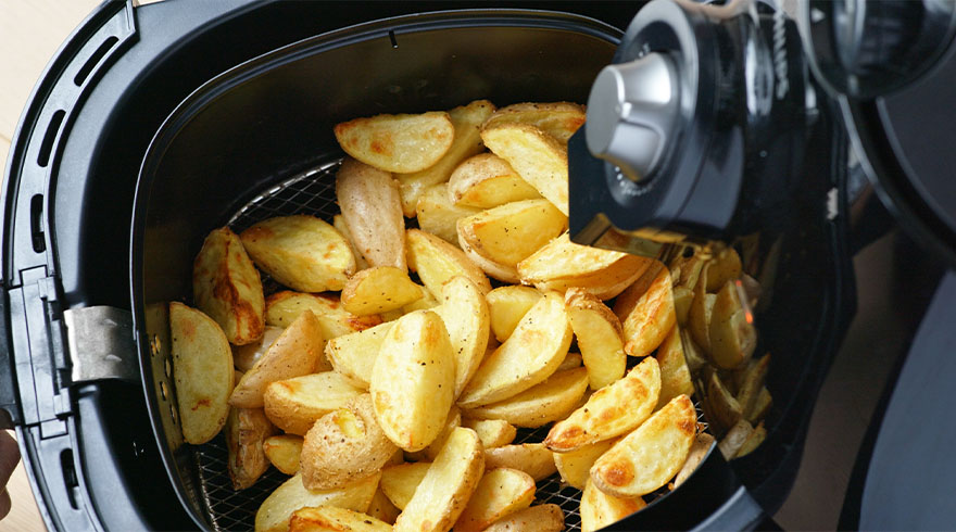 Een zwarte airfryer met goudbruine aardappelpartjes in een metalen mand.