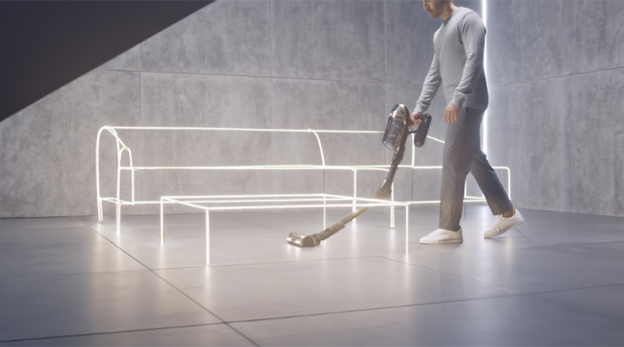 Een man stofzuigt een grijze vloer met een kruimeldief. Er staat een neon bankstel en tafel in de kamer.