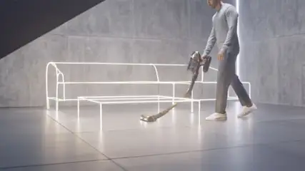 Een man stofzuigt een grijze vloer met een kruimeldief. Er staat een neon bankstel en tafel in de kamer.