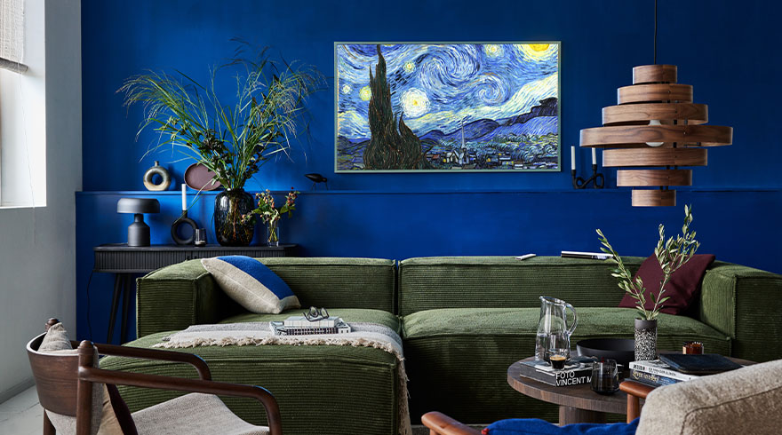 Een woonkamer met blauwe muren, een groene bank, een houten lamp en een schilderij van "De sterrennacht".