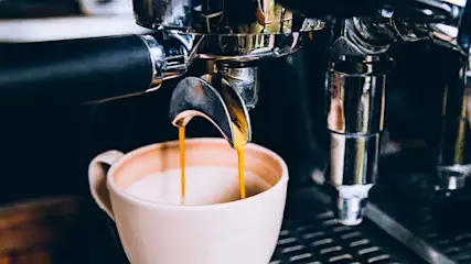 Espresso stroomt uit een zilverkleurige machine in een witte mok, op een donkere achtergrond.