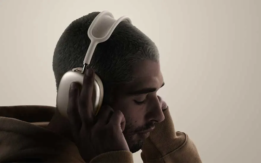 Zijaanzicht van een persoon met kort geschoren haar en hoodie die een beige hoofdtelefoon draagt, ogen dicht, verdiept in muziek op neutrale achtergrond.