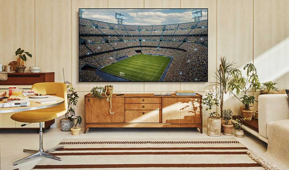 Een grote tv toont een vol voetbalstadion in een warme woonkamer met houten meubels en veel planten.