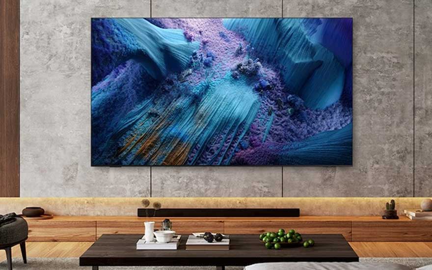In een stijlvolle woonkamer hangt een grote tv aan de muur, waarop een kleurrijk abstract kunstwerk of natuurdetail wordt getoond.