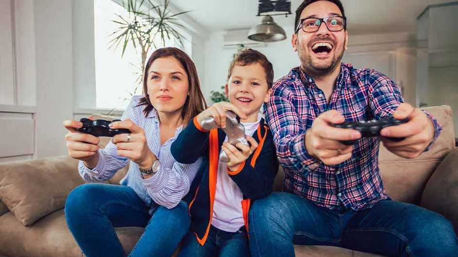 Een gezin zit op een bank en speelt videogames met controllers in hun handen.
