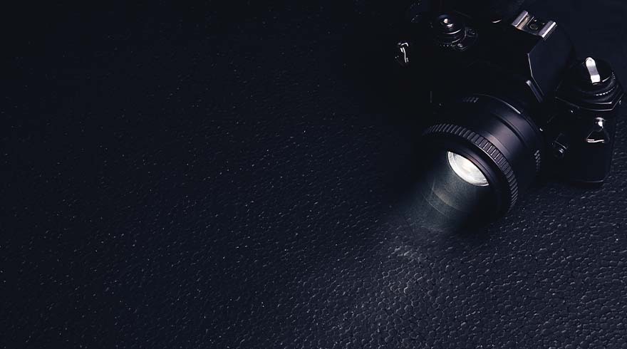 Een zwarte camera met een lens staat rechtsboven op een donkere, korrelige achtergrond.