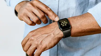 Een pols met een zwart horloge wordt aangeraakt door een vinger, tegen een vage achtergrond.