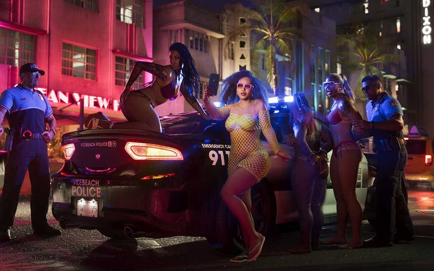 In a neon-lit night city, women in striking outfits pose by a police car with flashing lights and watching officers.