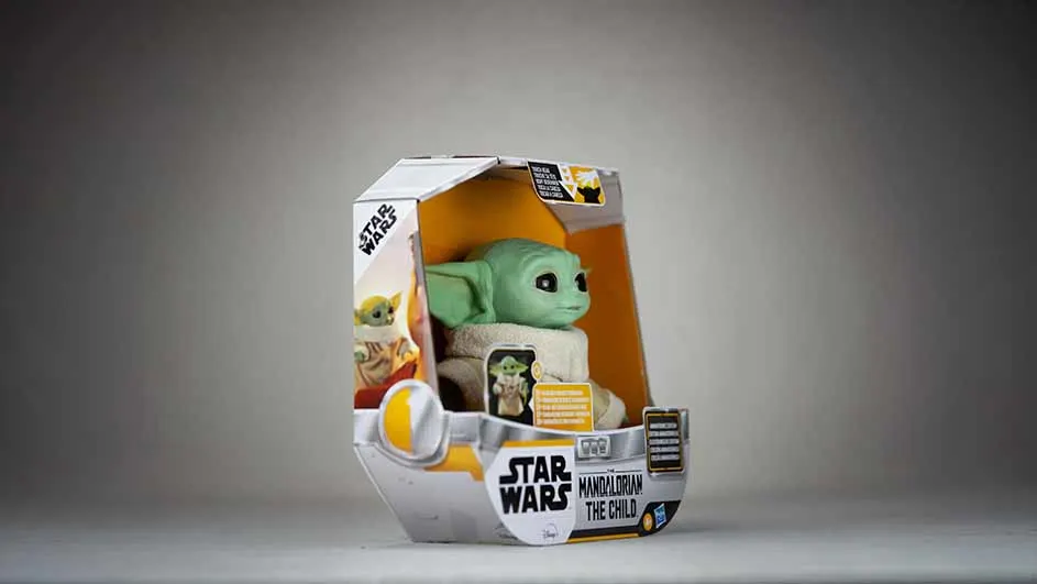 Een Grogu-figuur in een doos, met Star Wars-logo's, op een grijze achtergrond.