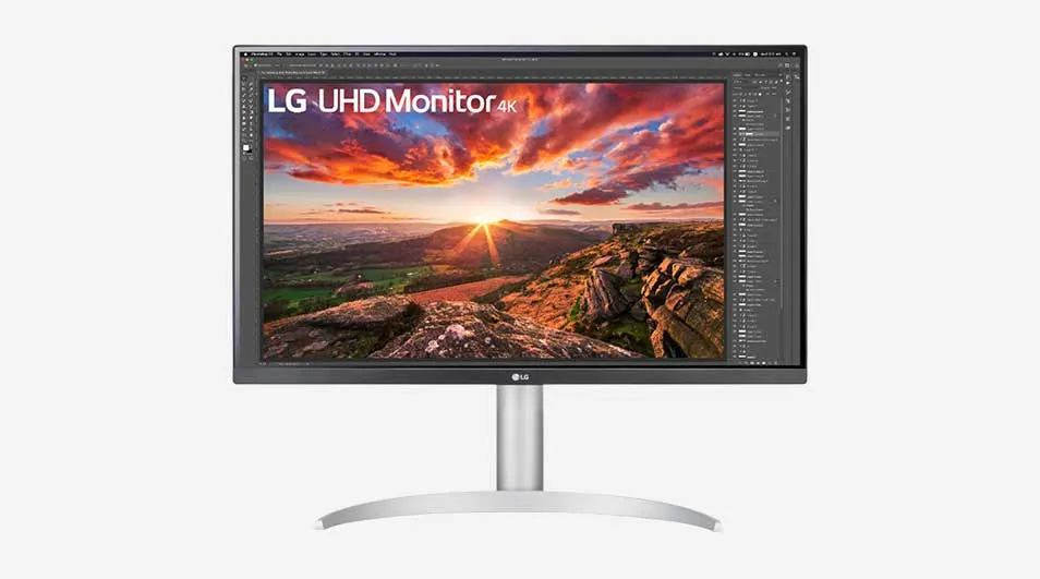 Een dunne LG UHD 4K-monitor toont een kleurrijke zonsondergang boven rotsachtige heuvels, omgeven door panelen van fotobewerkingssoftware.