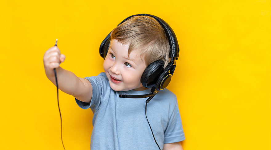 Een jongen met een grijs shirt en een zwarte hoofdtelefoon houdt een kabel vast tegen een gele achtergrond.