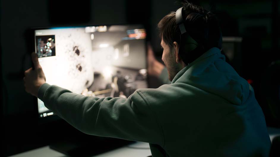 Een man met een koptelefoon speelt een computerspel op een groot scherm in een donkere kamer.