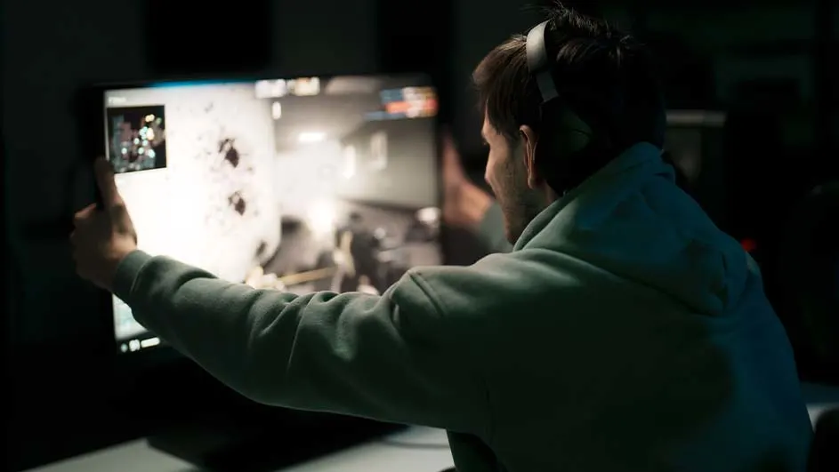 Een man met een koptelefoon speelt een computerspel op een groot scherm in een donkere kamer.