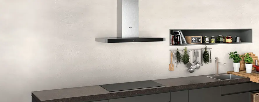 Een keuken met een zilveren afzuigkap, een ingebouwde plank met spullen, keukengerei, kruiden en twee planten in witte potten.