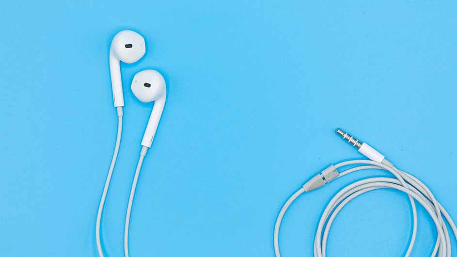 Witte oortjes met snoer en een witte audiostekker liggen op een blauwe achtergrond.